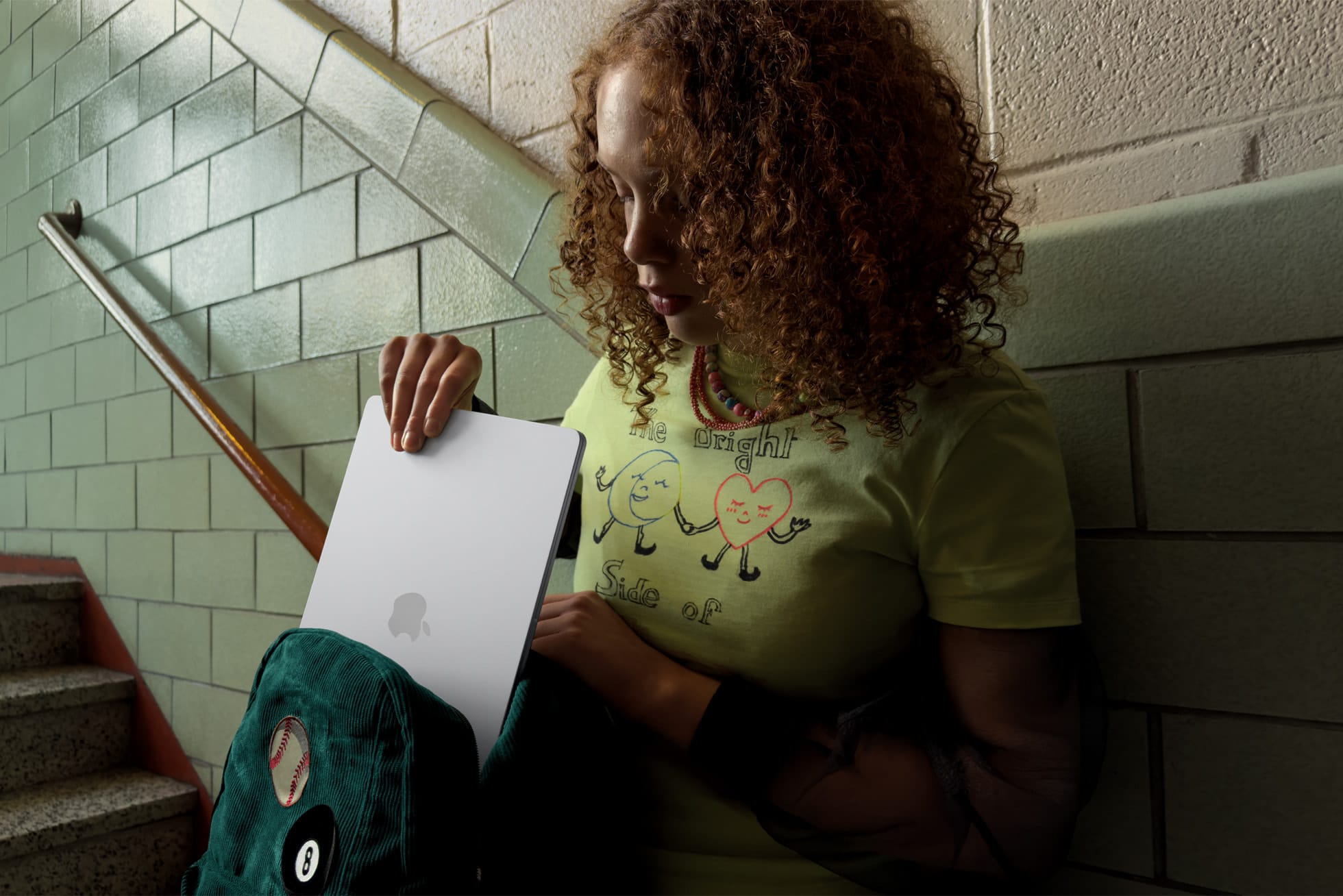 Young person retrieving an Apple MacBook Air from a backpack in a school setting.