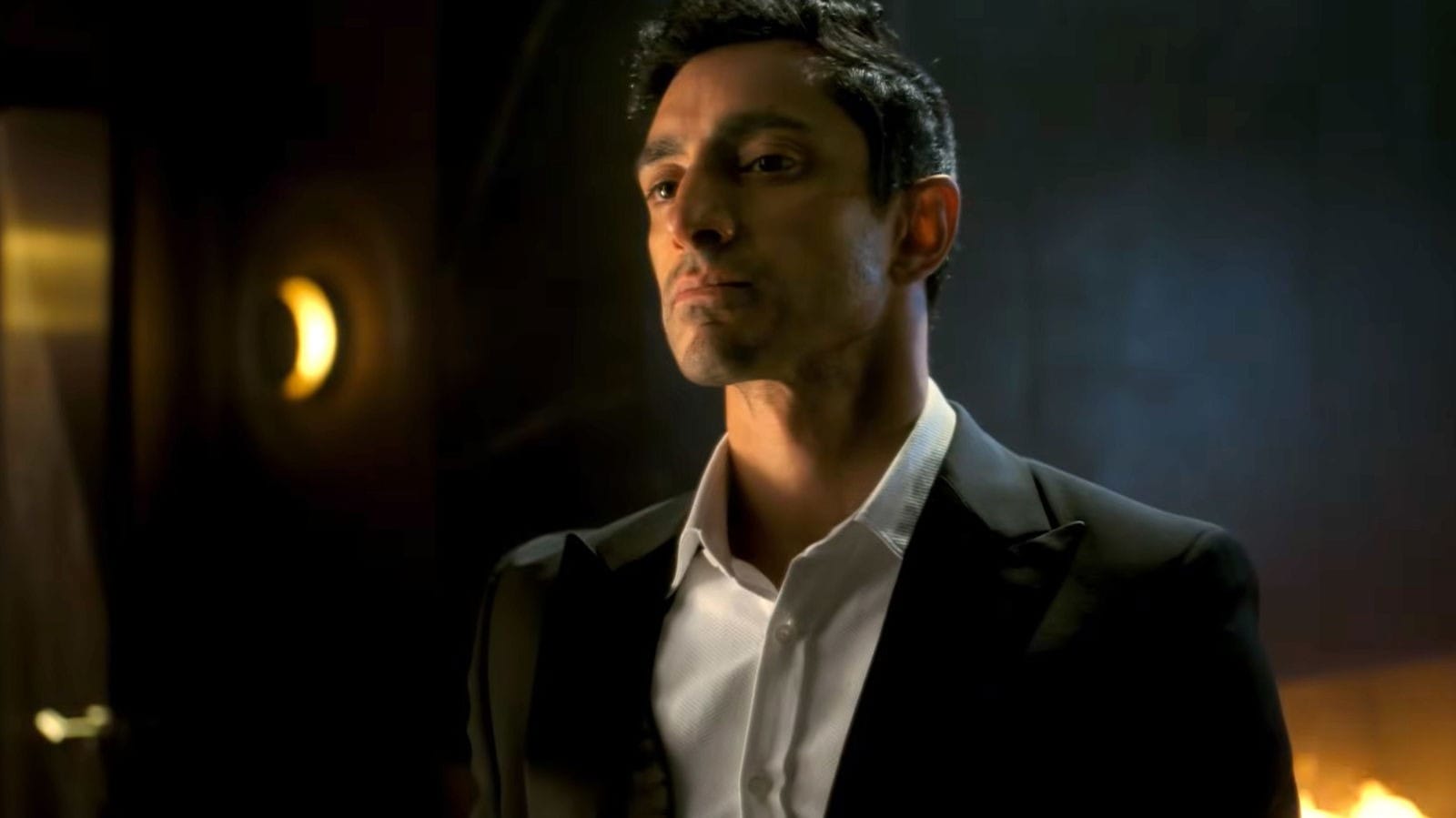 A man in a tuxedo looking serious, set against a dimly lit background