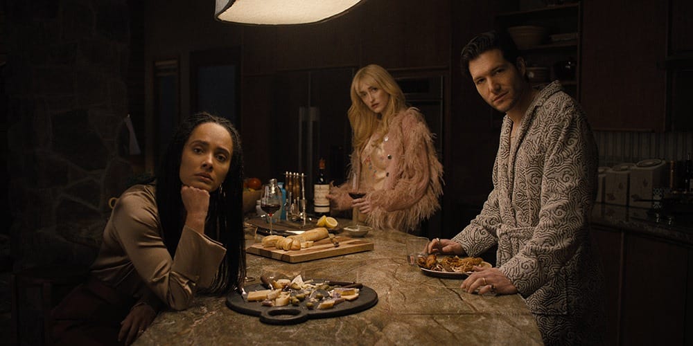 Three characters in a kitchen, with a table full of food and drinks