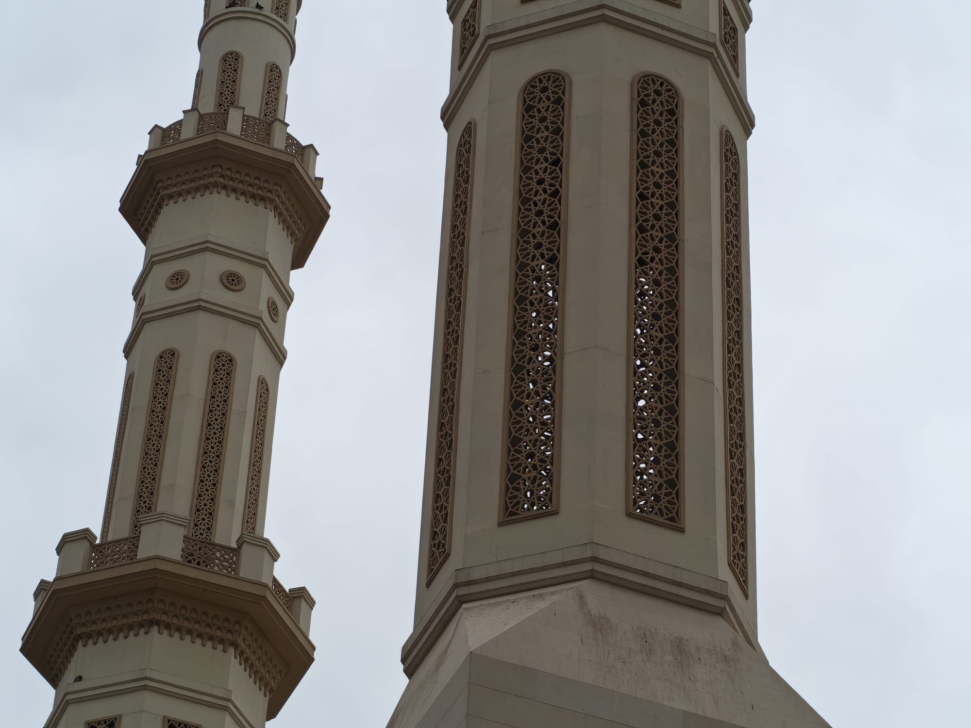 Honor 600 daylight camera sample: two beige minarets with intricate latticework against an overcast sky