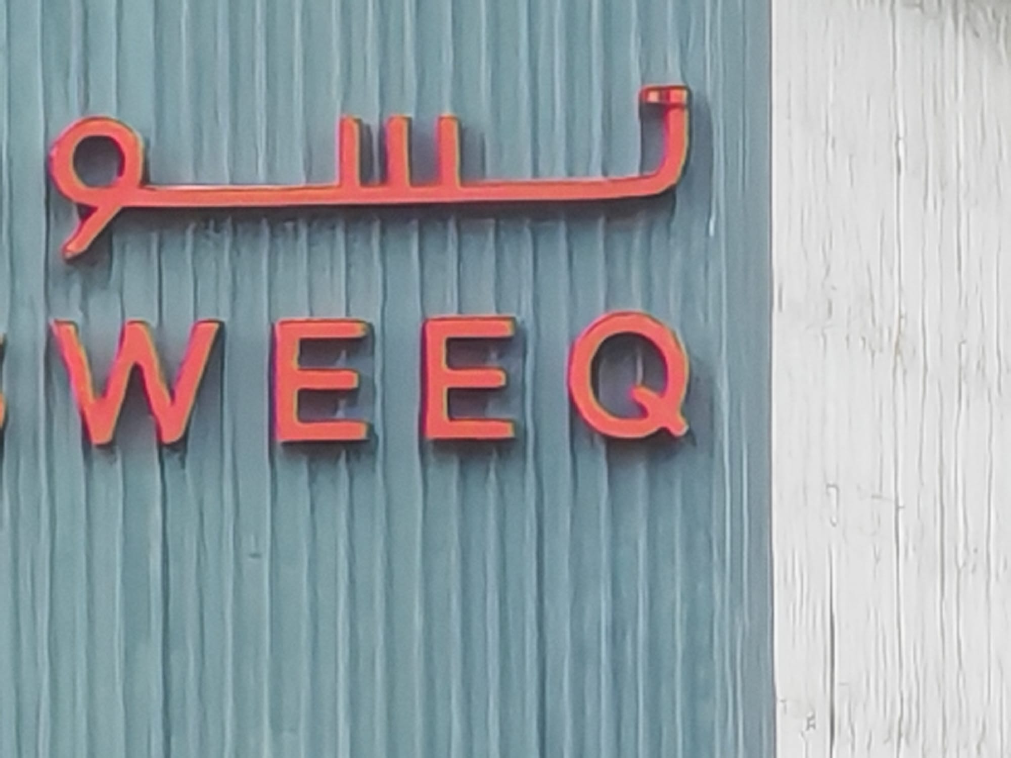 Honor 600 close-up camera sample: red "WEEQ" signage in English and Arabic on a teal corrugated panel