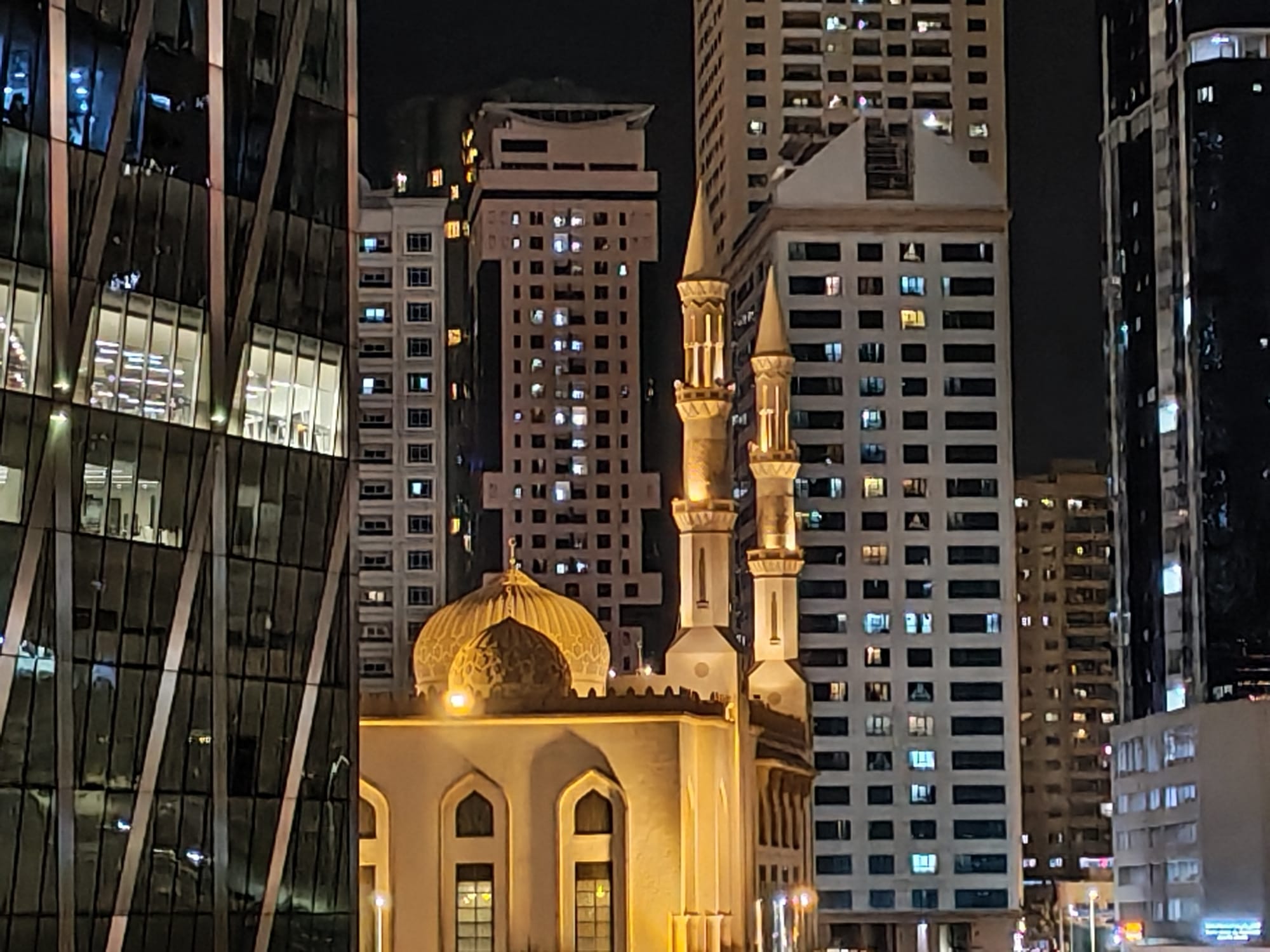 Honor 600 night zoom camera sample: a small illuminated mosque framed by glass office and apartment towers