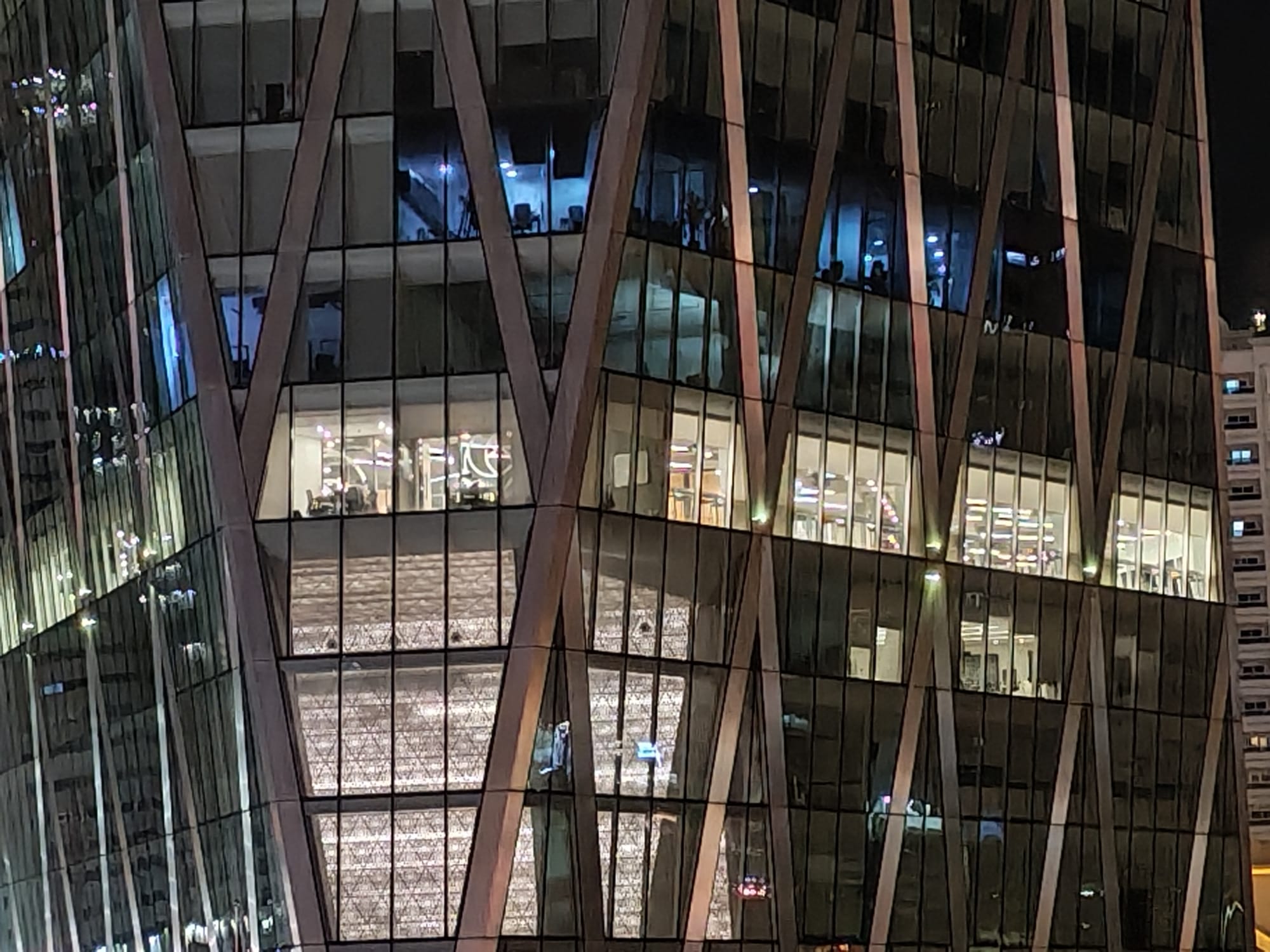 Honor 600 night zoom camera sample: glass office tower facade with illuminated interiors and diagonal structural beams