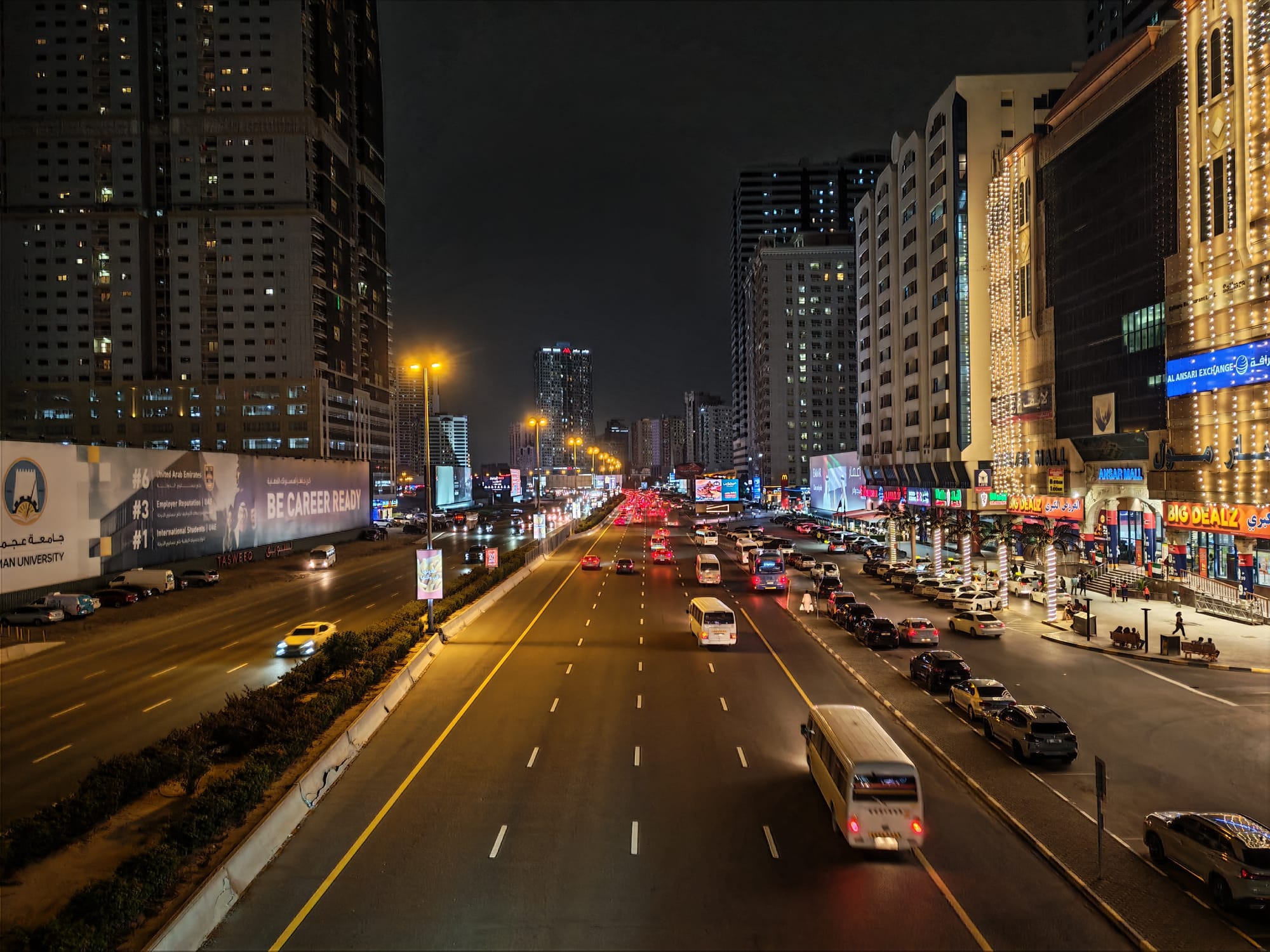 Honor 600 night camera sample: multi-lane Sharjah road with traffic, billboards, and palm-lit shopfronts