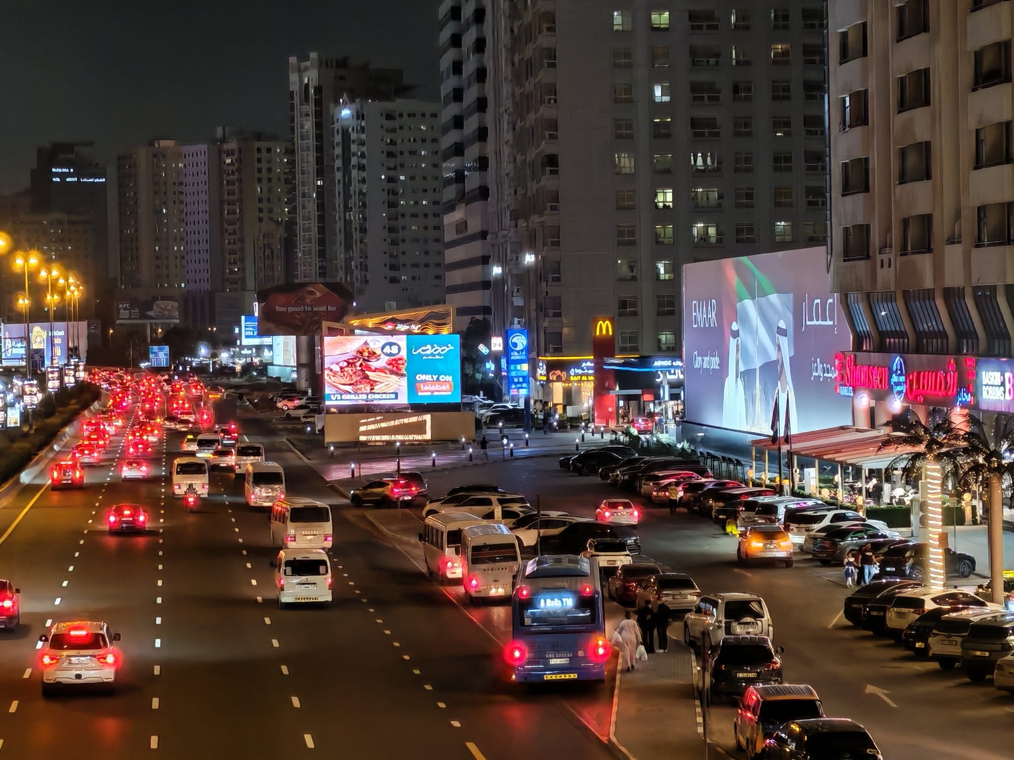 Honor 600 night camera sample: dense Sharjah road junction with car taillights, billboards, and storefront signage