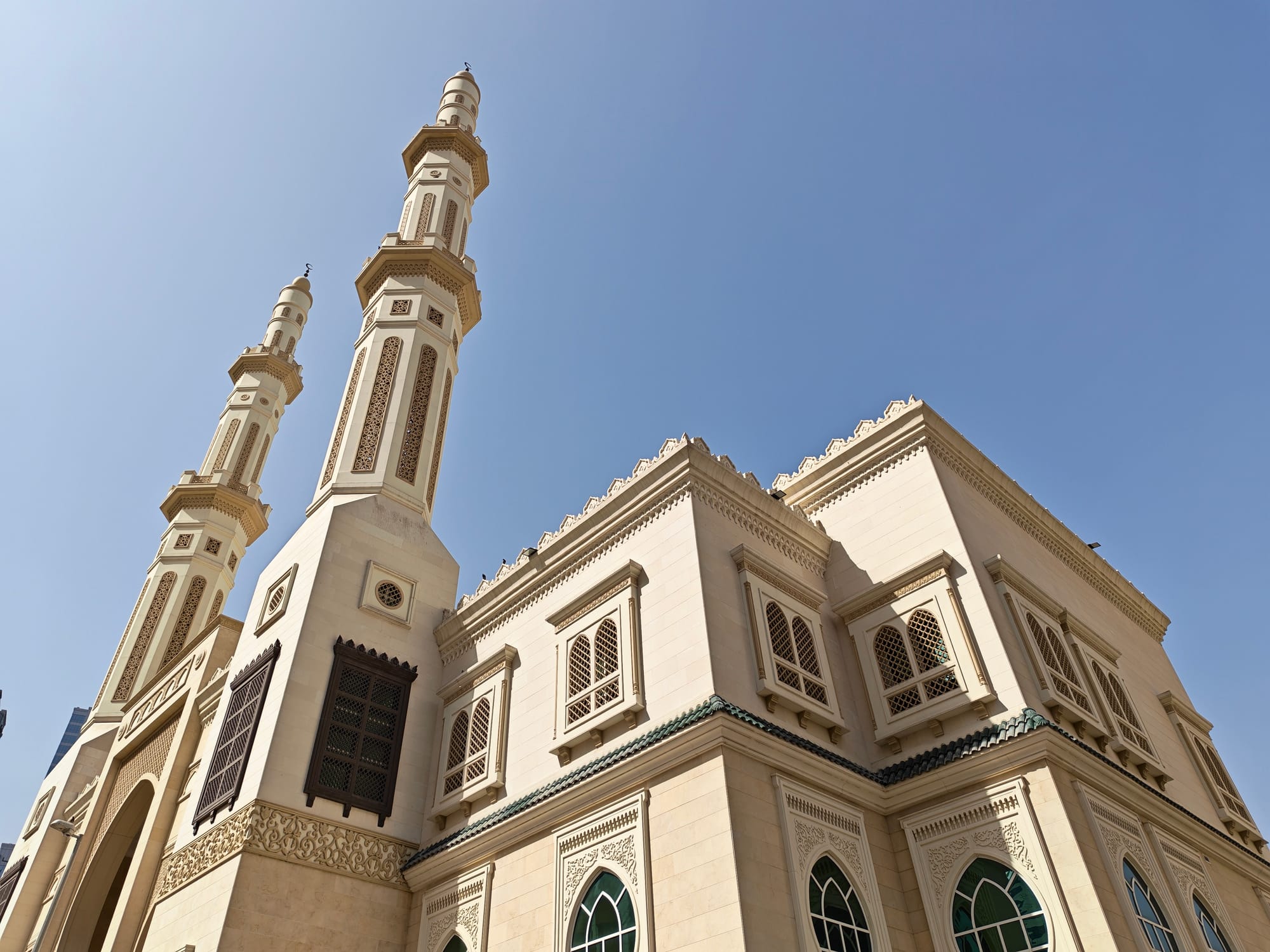 Tall mosque with twin minarets and ornate architecture against a blue sky.