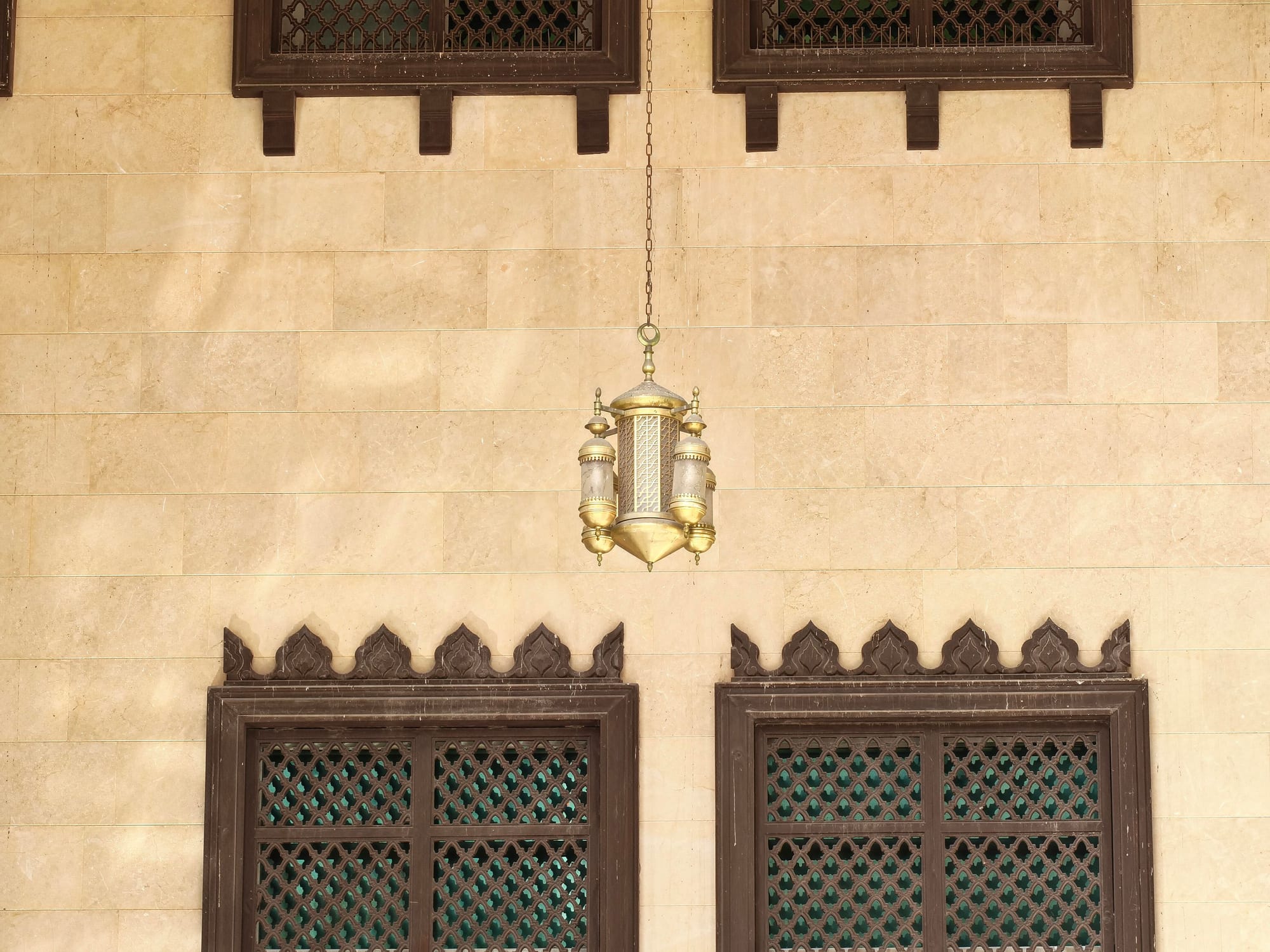 Decorative lantern hanging between mosque windows with patterned screens.