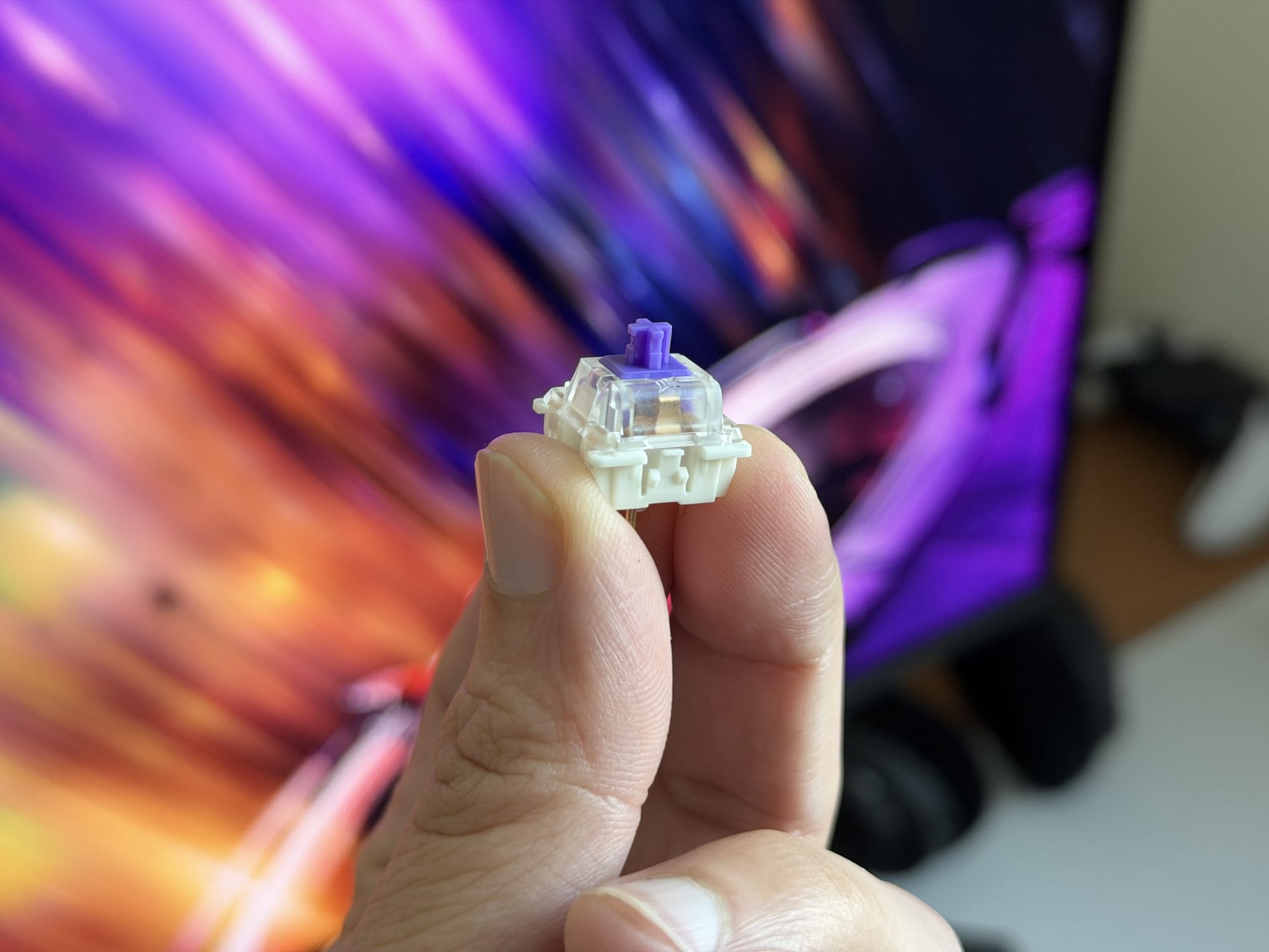 RGB keyboard switch held in hand, showcasing detailed structure and purple stem.