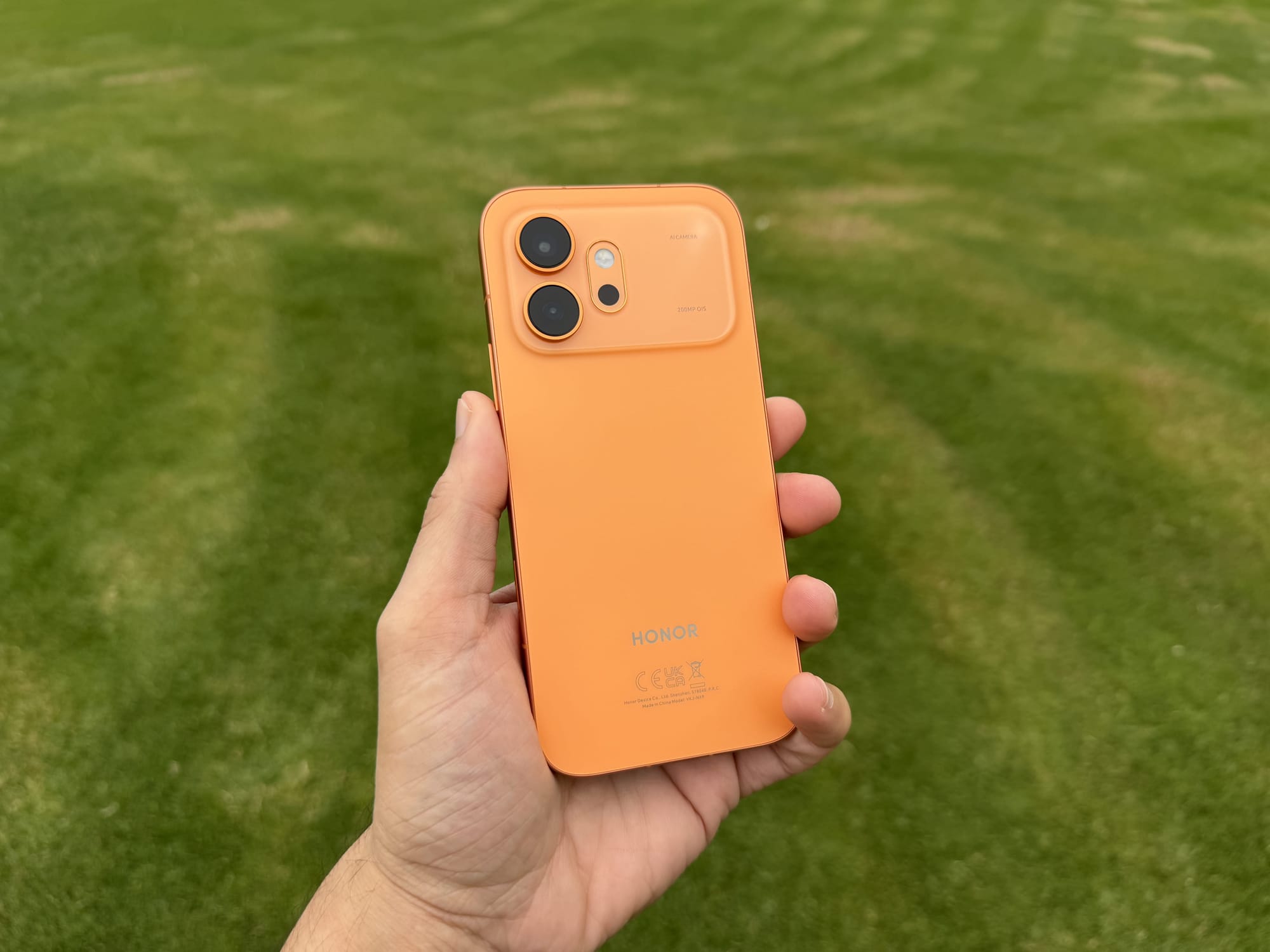 Rear of the Honor 600 in orange held in hand, showing the camera island and Honor logo on the back