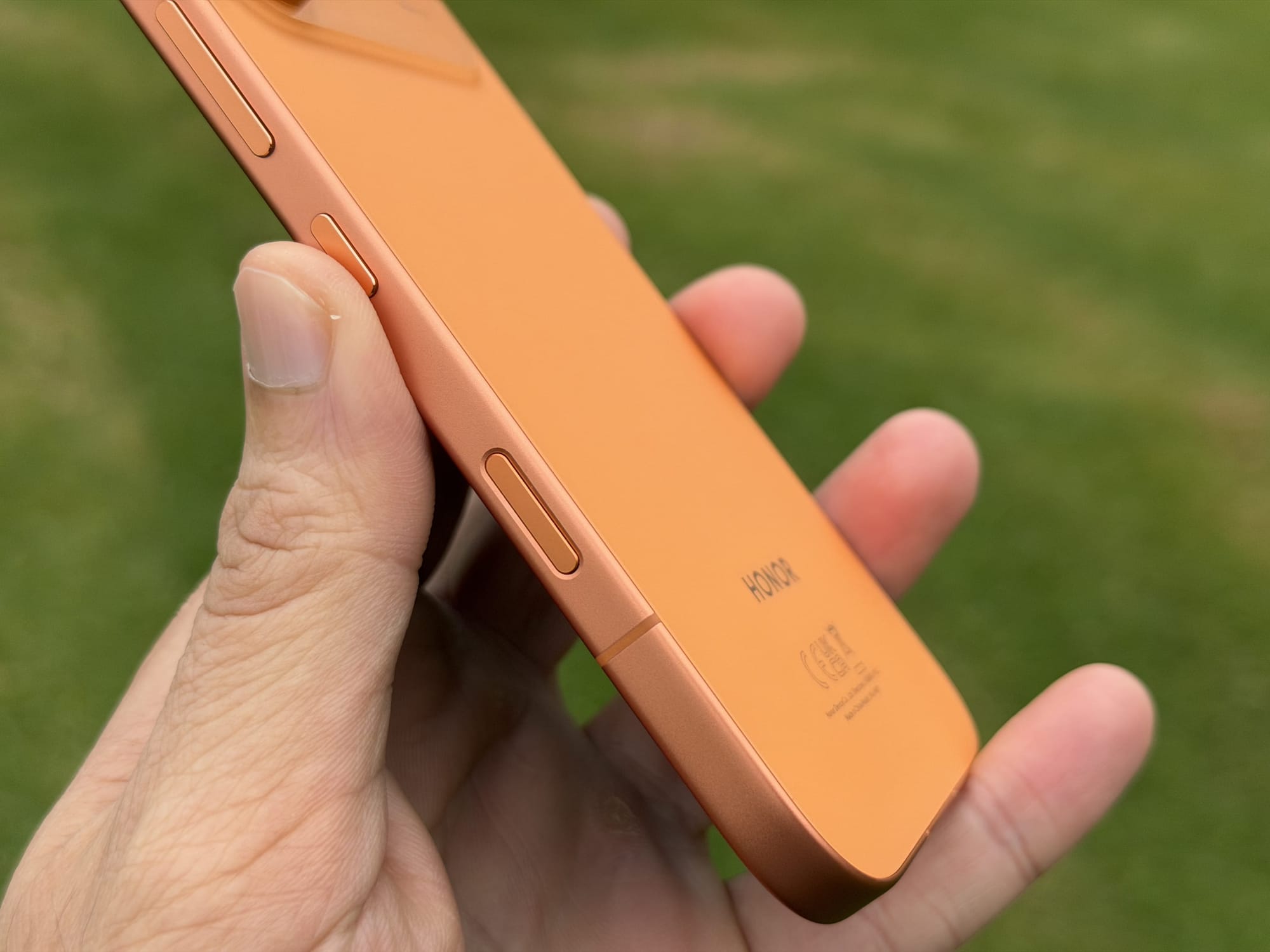 Side profile of the Honor 600 in orange held in hand, showing the volume rocker and power button along the frame