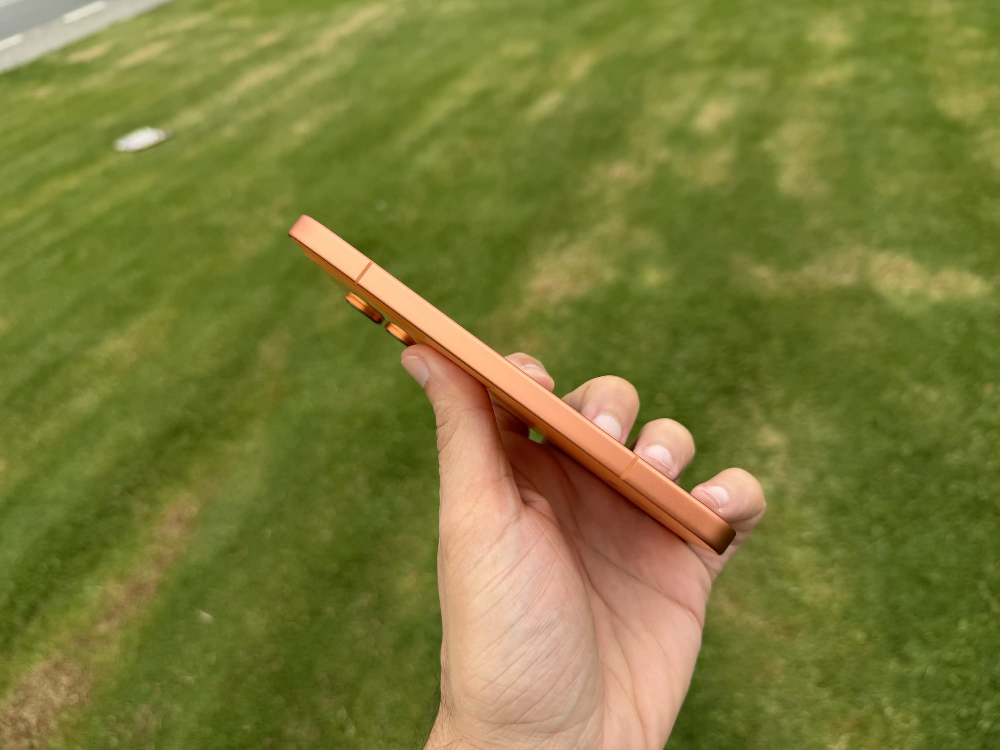 Bottom edge of the Honor 600 in orange held in hand, showing the slim profile and antenna lines