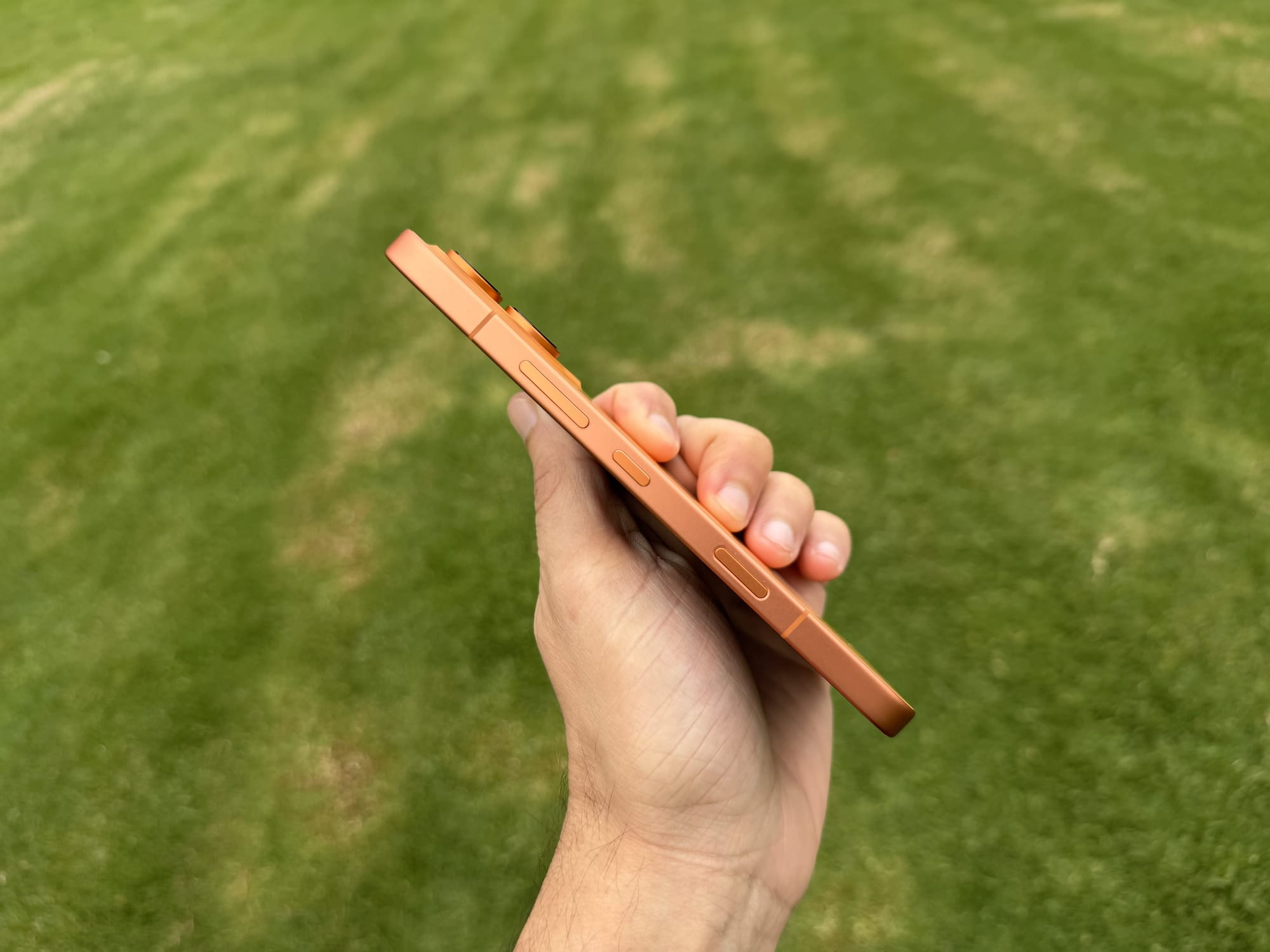 Top edge of the Honor 600 in orange held in hand, showing the camera bump and side controls