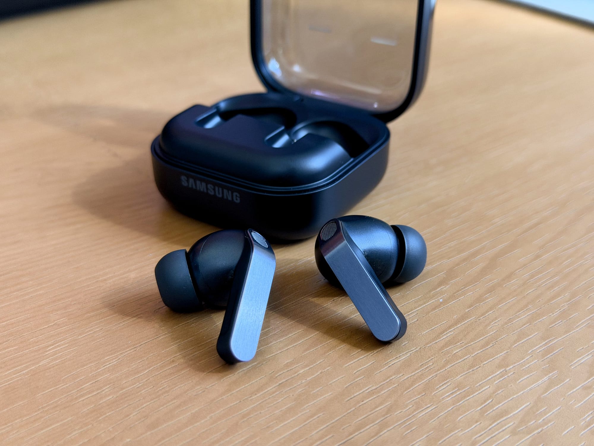 Samsung Galaxy Buds4 Pro earbuds outside the charging case on a wooden surface.
