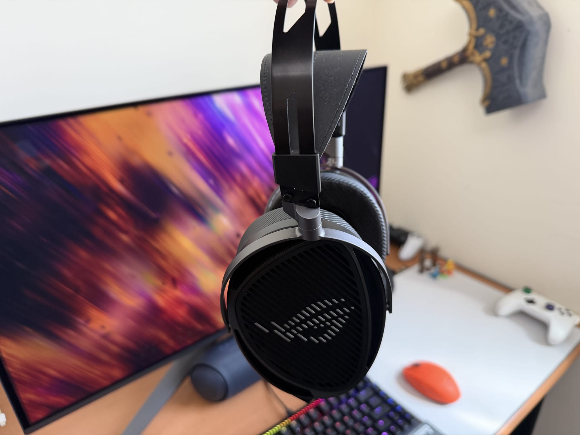 Asus ROG Kithara headset hanging from a mount, with a monitor in the background.