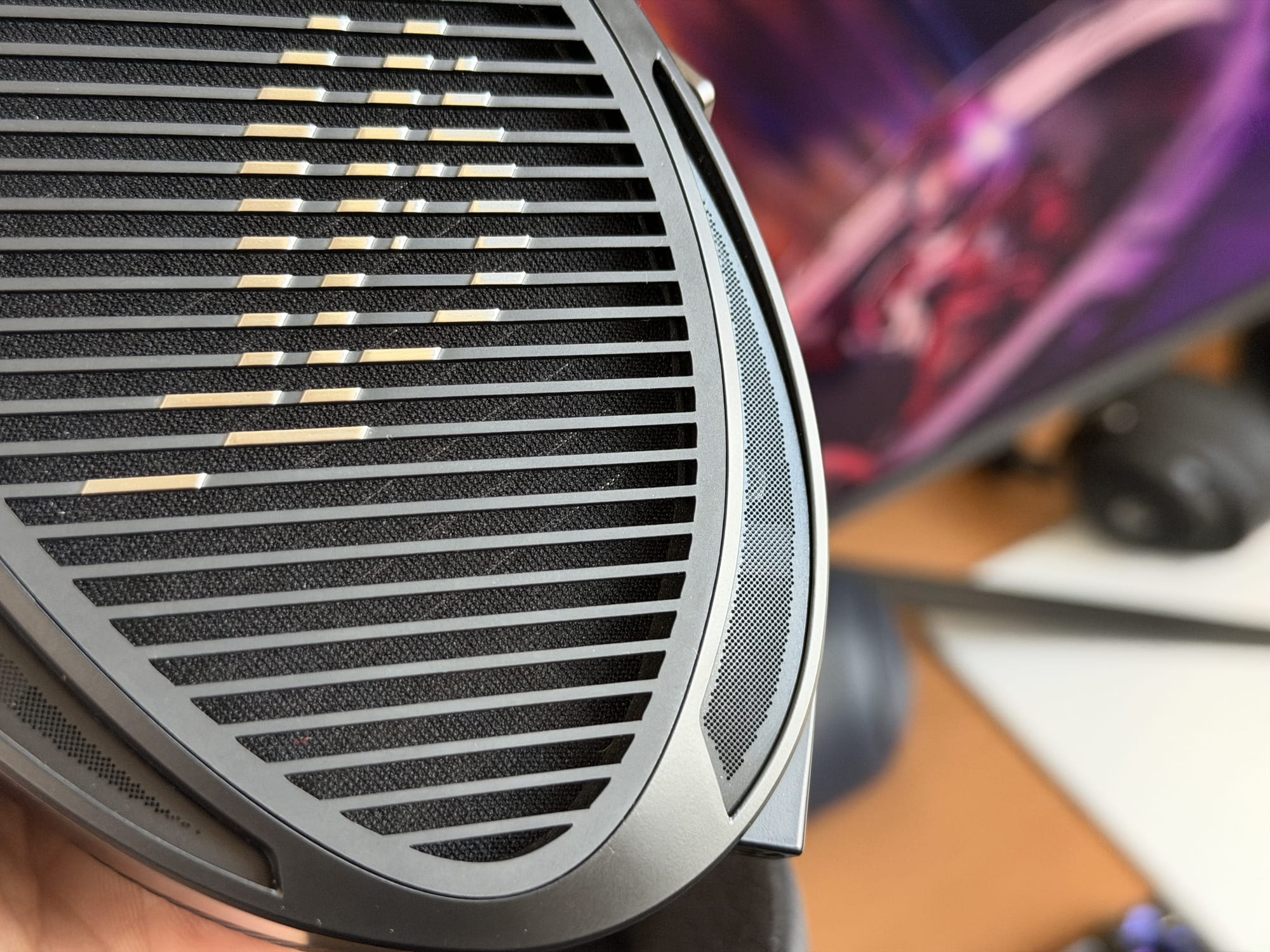 Close-up of the earcup grille of the Asus ROG Kithara headset with a colorful monitor in the background.