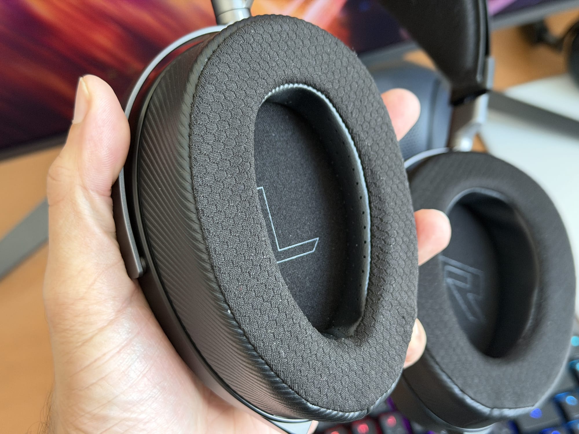 Hand holding the ear cushion of the Asus ROG Kithara headset, highlighting comfort design.