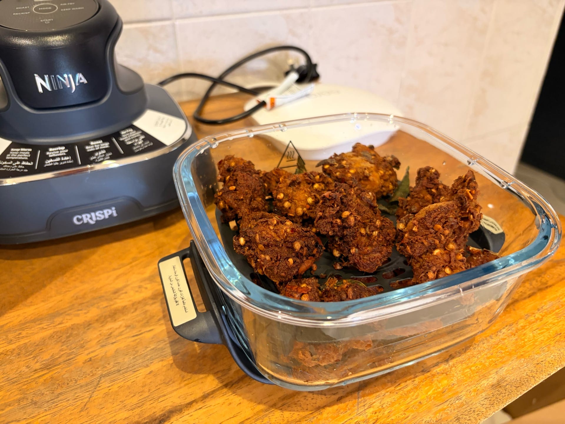 Golden brown chicken pieces cooked in the Ninja Crispi, presented in a glass container