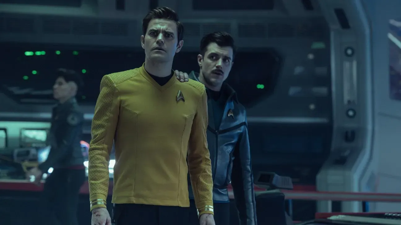 Two characters in Starfleet uniforms react with concern aboard the starship.