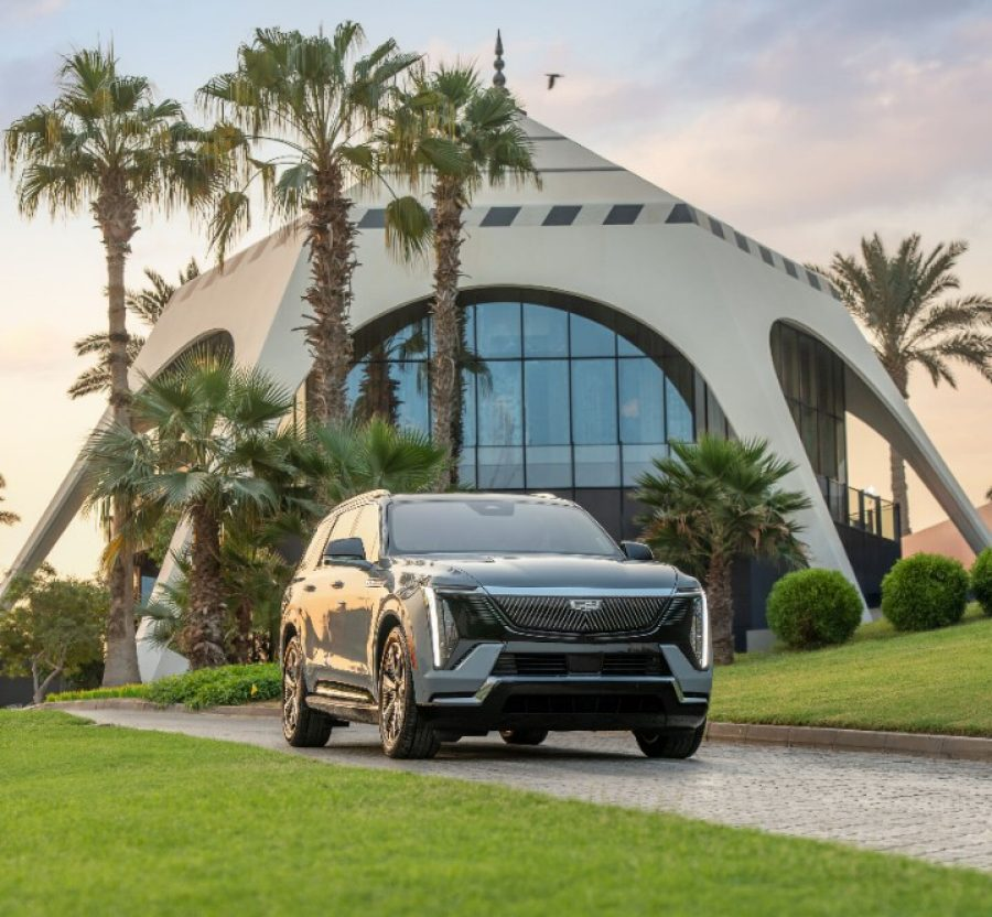 Cadillac Escalade IQ parked on a pathway surrounded by palm trees and a modern building.
