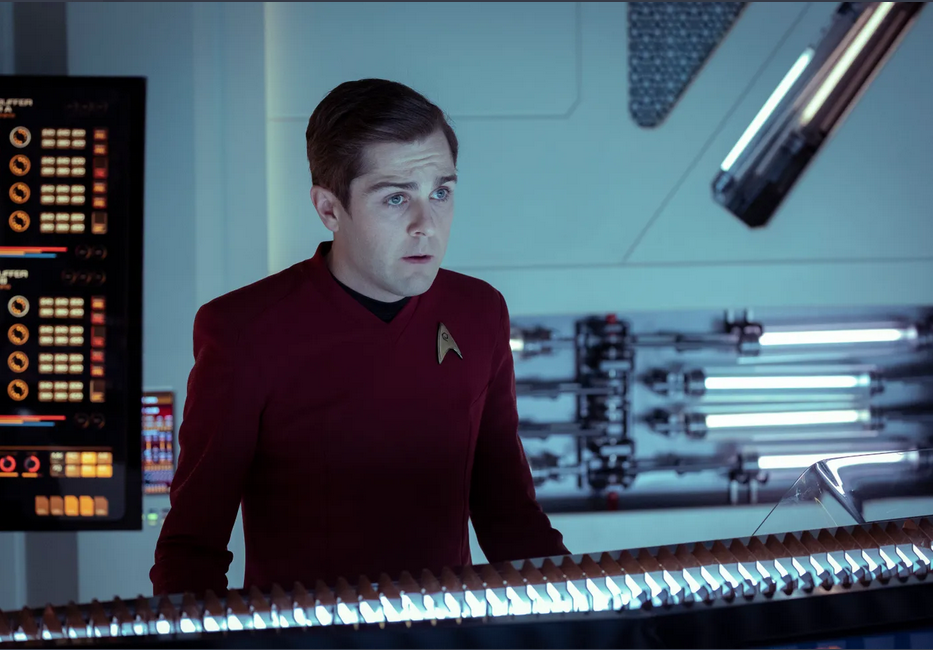 A character in a red Starfleet uniform stands at a control panel, appearing focused.