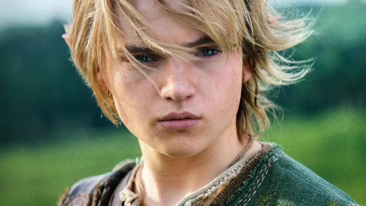 Link character from Legend of Zelda movie with blonde hair and serious expression set against a green landscape.