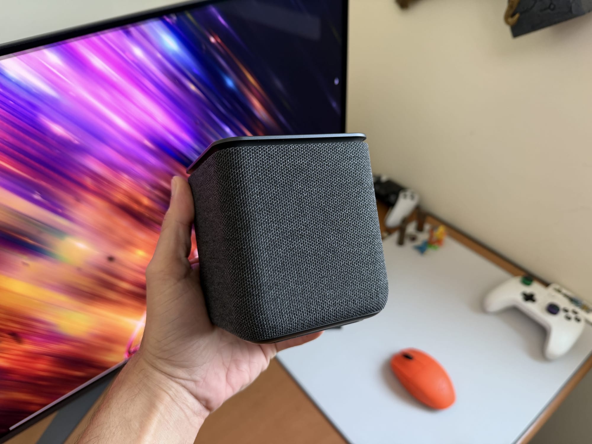 Yasmina Midi smart speaker held in a hand with vibrant background.