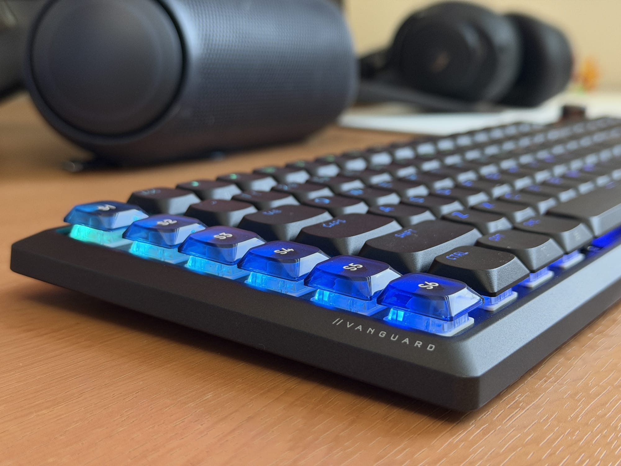 Corsair Vanguard Air 99 keyboard with blue LED lighting on keys, placed beside speakers and headphones.