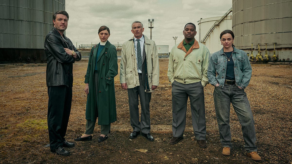 Five main characters stand together in an industrial setting, each in distinct outfits.