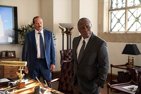 Two men in suits standing in an office, one looking serious while the other seems contemplative.