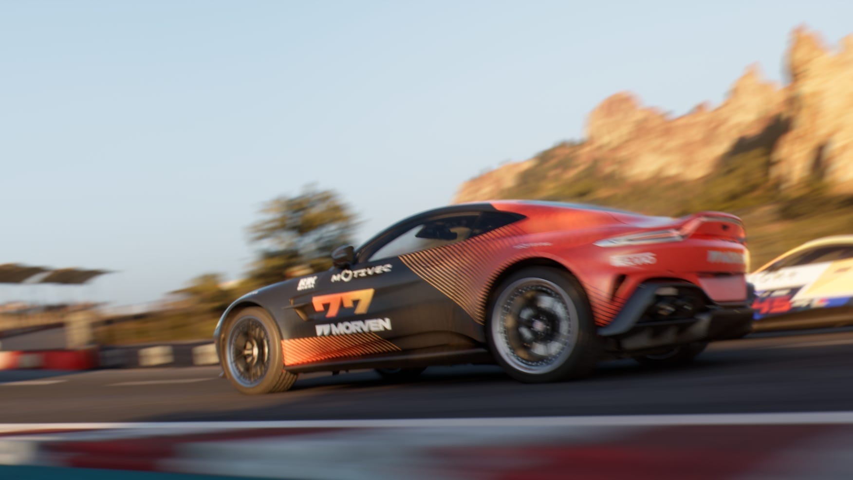 A dynamically blurred orange sports car racing on a track, set against rocky hills.