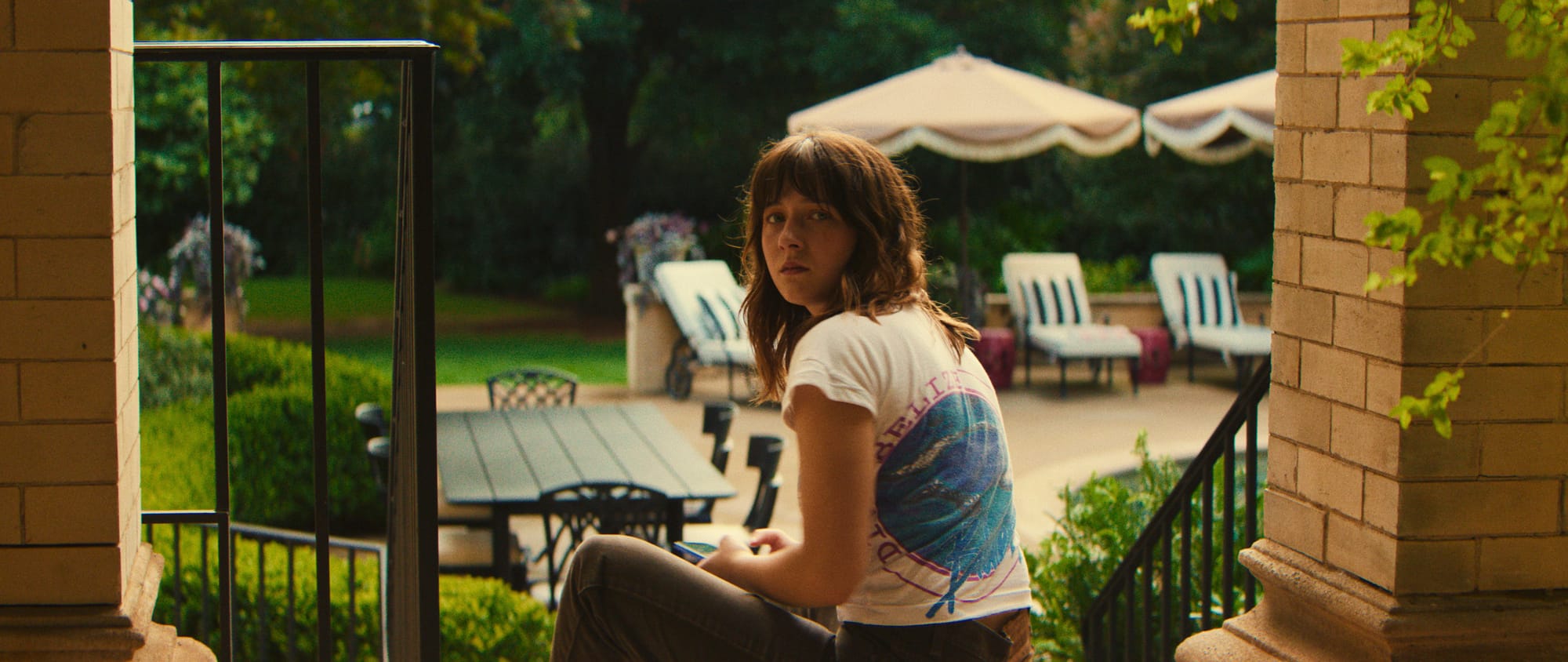 A young woman sitting on a staircase, looking back while holding a notebook in a garden.