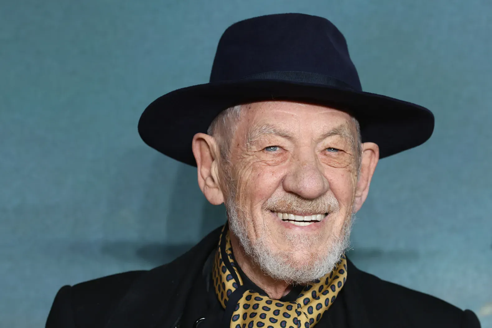 Ian McKellen wearing a black hat and scarf, smiling at a premiere.