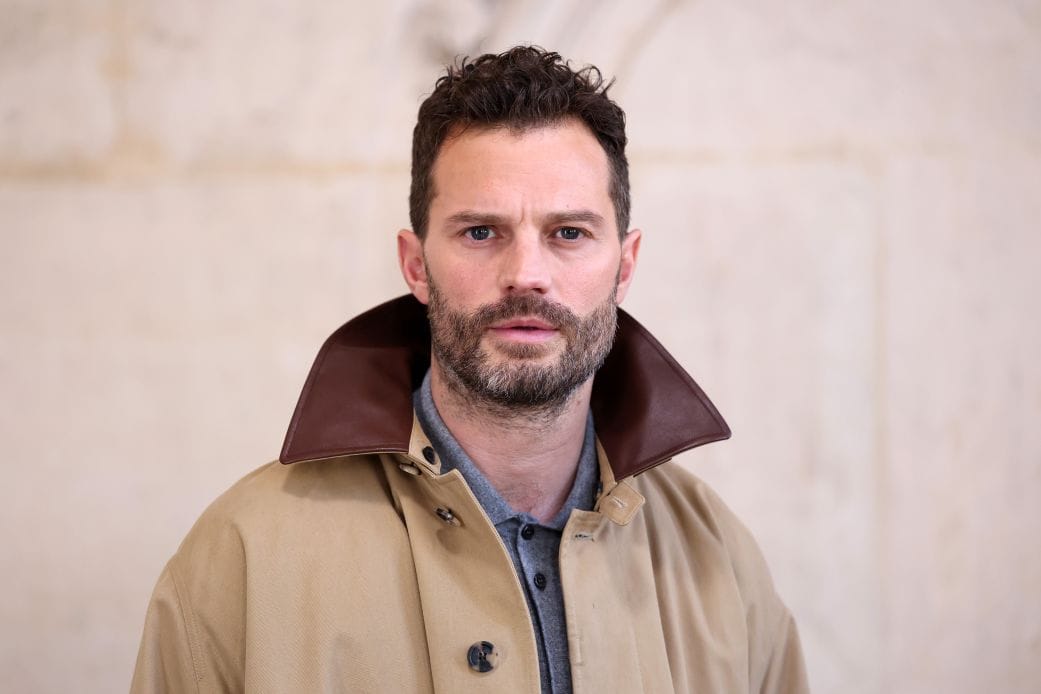 Jamie Dornan posing in a beige coat with a brown collar.