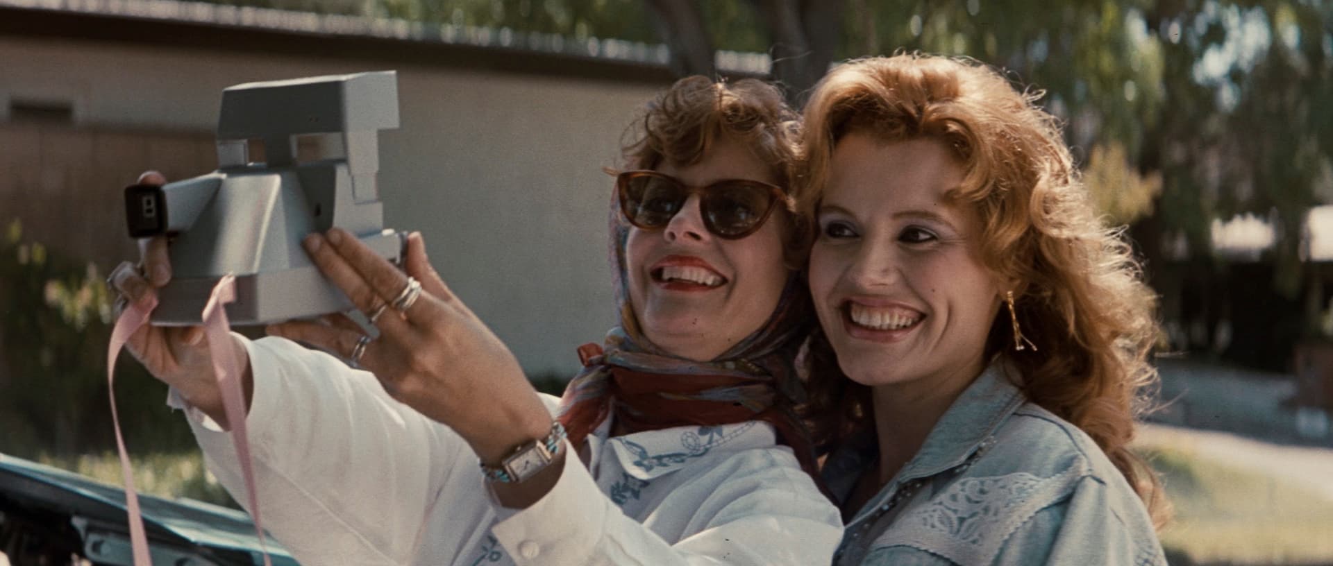 Susan Sarandon and Geena Davis smiling and taking a selfie in Thelma & Louise, showcasing their friendship.