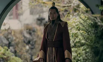 A character in a red robe stands in a traditional Asian setting surrounded by greenery.