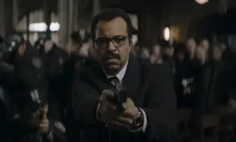 Jeffrey Wright in character holding a gun, surrounded by a crowd of police officers in dark surroundings.