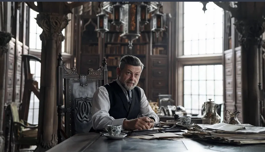 Sean Bean seated at an ornate wooden desk, surrounded by clutter.
