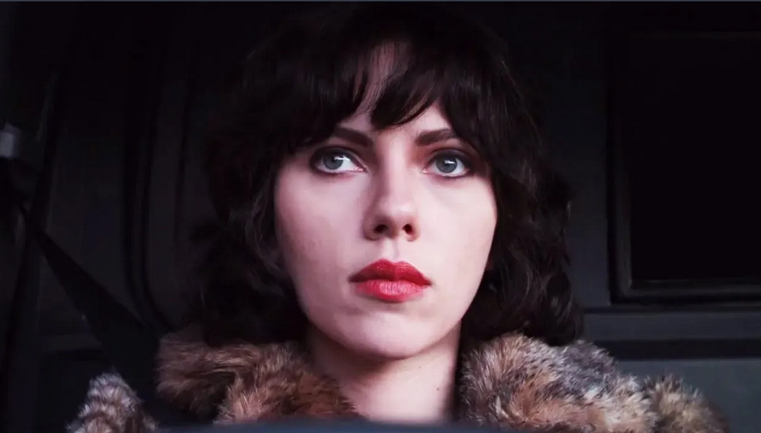 Scarlett Johansson with styled hair and dramatic makeup, sitting in a vehicle.
