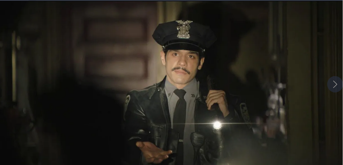 A policeman with a mustache and leather jacket, holding a flashlight and looking serious.