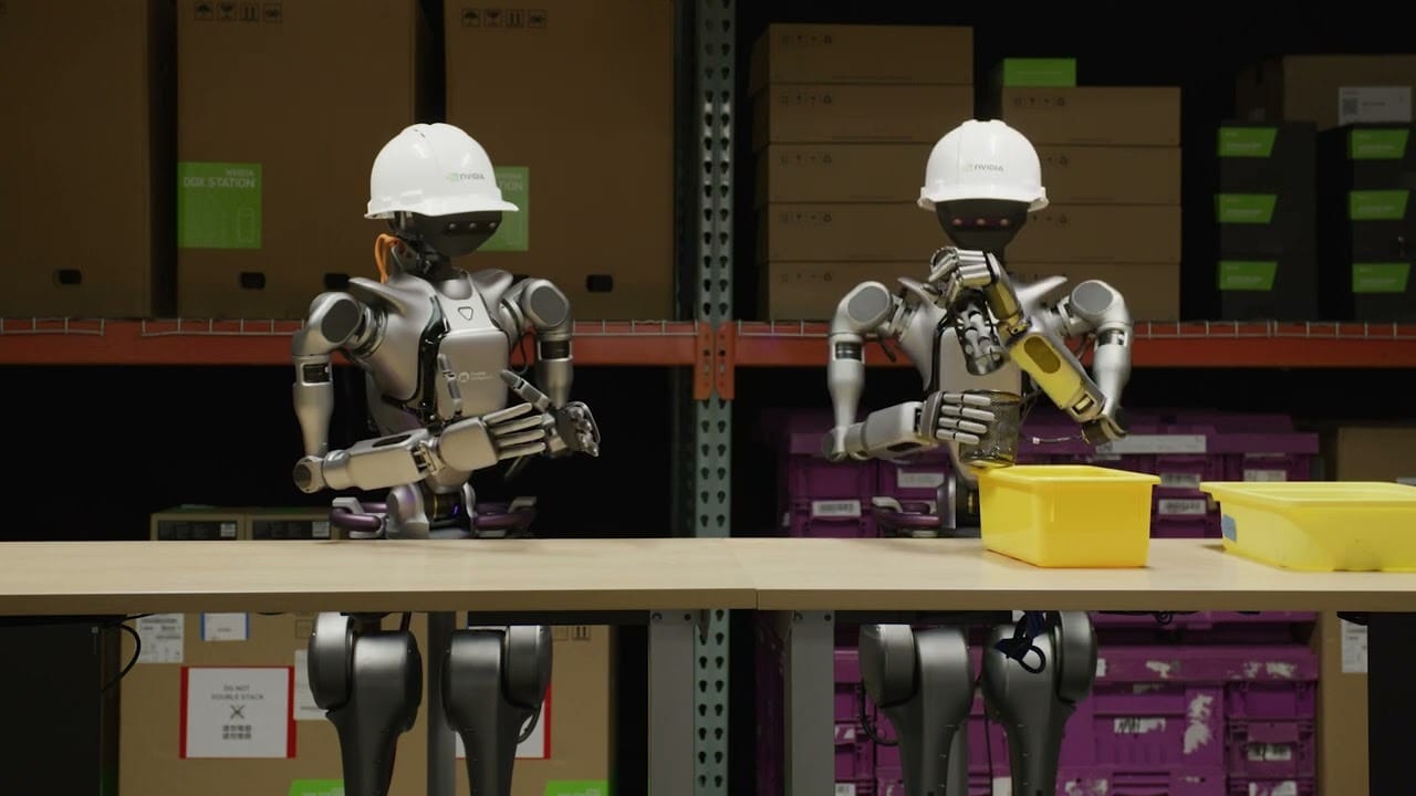 Two humanoid robots in hard hats working on a tabletop in a storage facility
