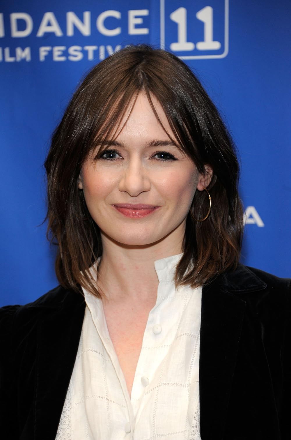 Emily Mortimer smiles at the Sundance Film Festival, wearing a black jacket against a blue backdrop.