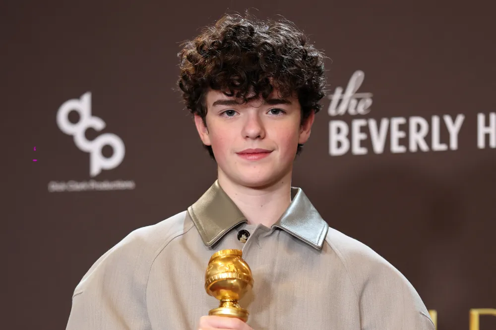 Owen Cooper holding a Golden Globe award, wearing a beige jacket, at an event backdrop in Beverly Hills.