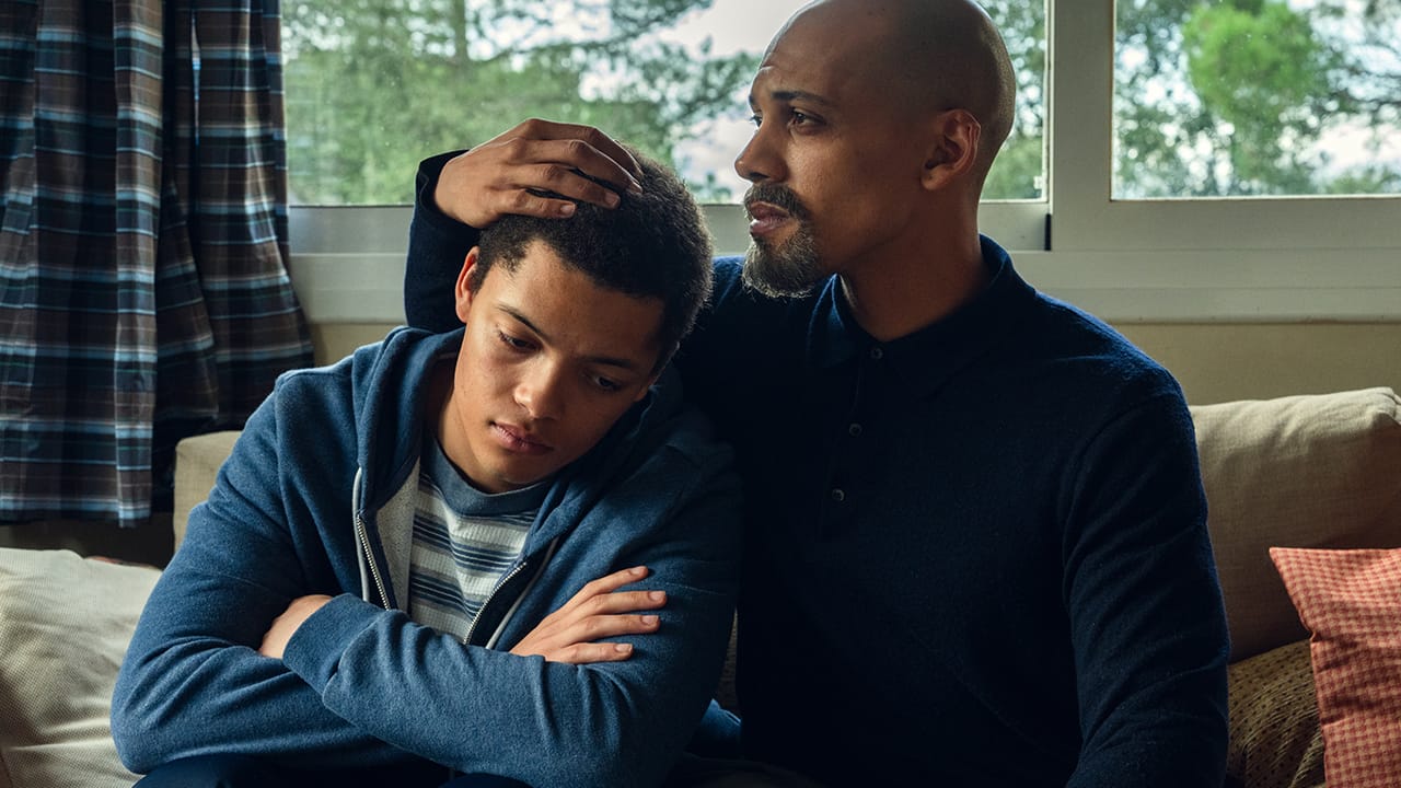 Emotional moment between a father and son sitting on a couch in a cozy setting.