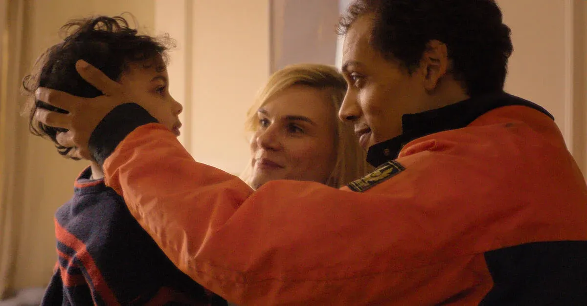 Family scene in 'The Witness' with a child being held by a woman and a man indoors.