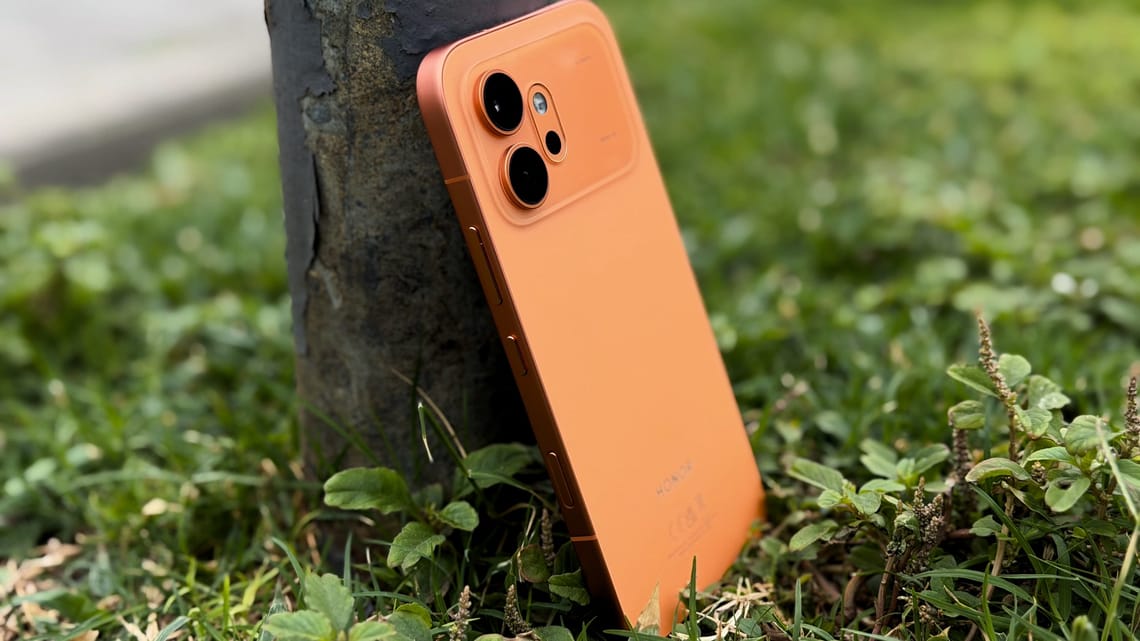 Honor 600 in orange propped against a tree trunk on grass, rear camera module visible