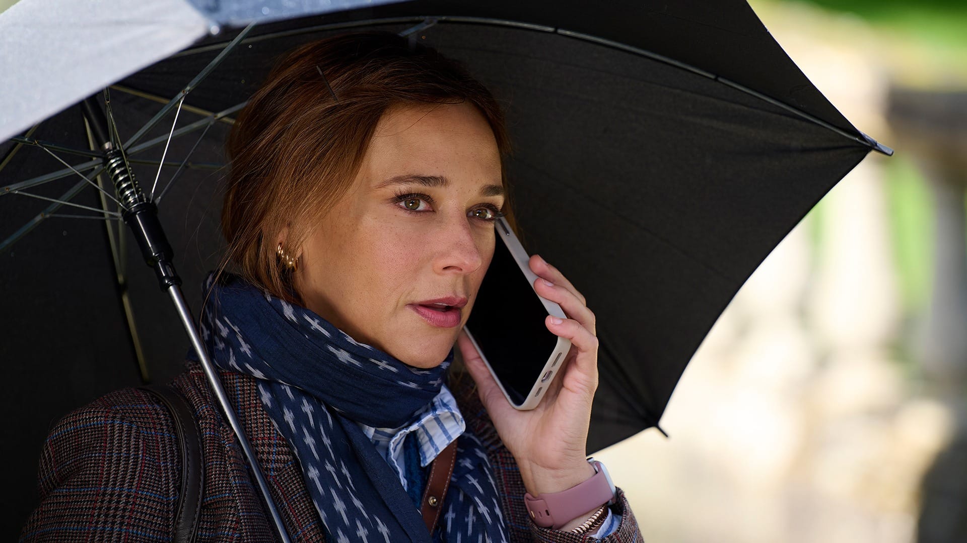 Woman speaking on the phone while holding an umbrella, looking concerned.