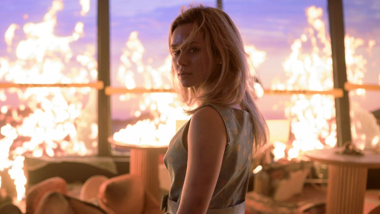 Woman in a reflective dress amidst a burning scene in a luxurious setting.