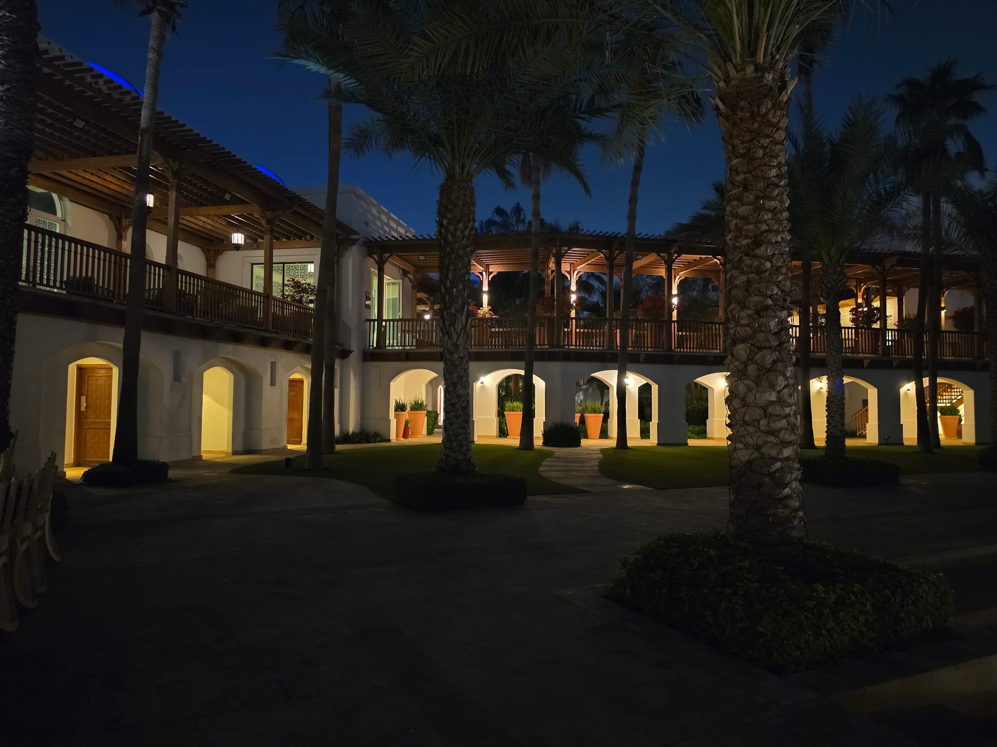 Night view of a courtyard with palm trees and illuminated architecture