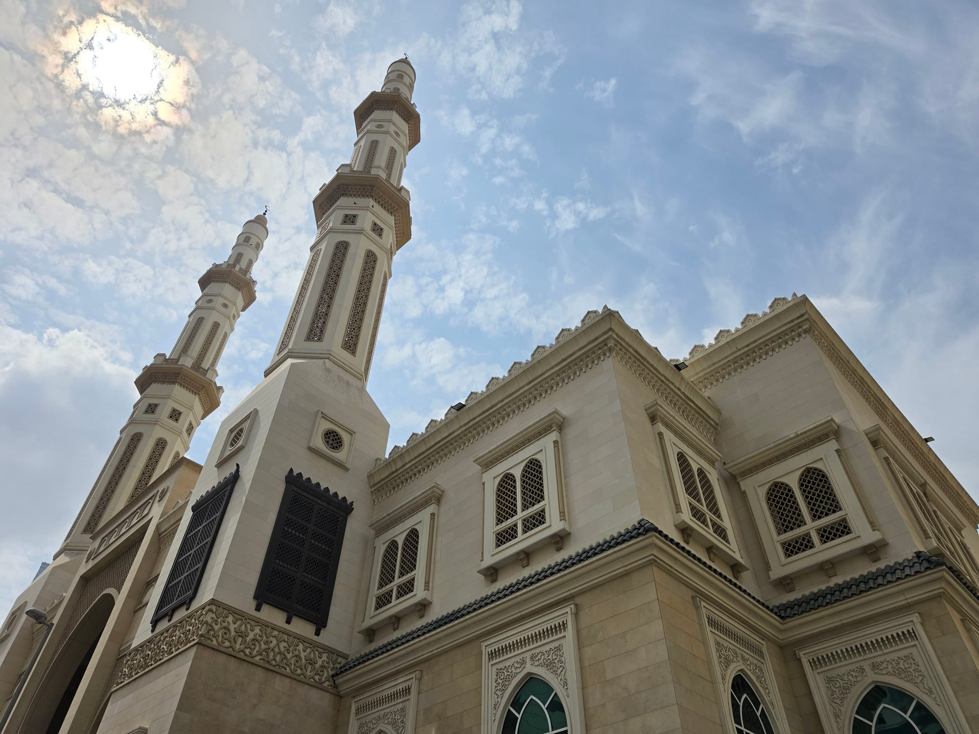 Architectural shot of a mosque with two tall minarets under a partly cloudy sky.
