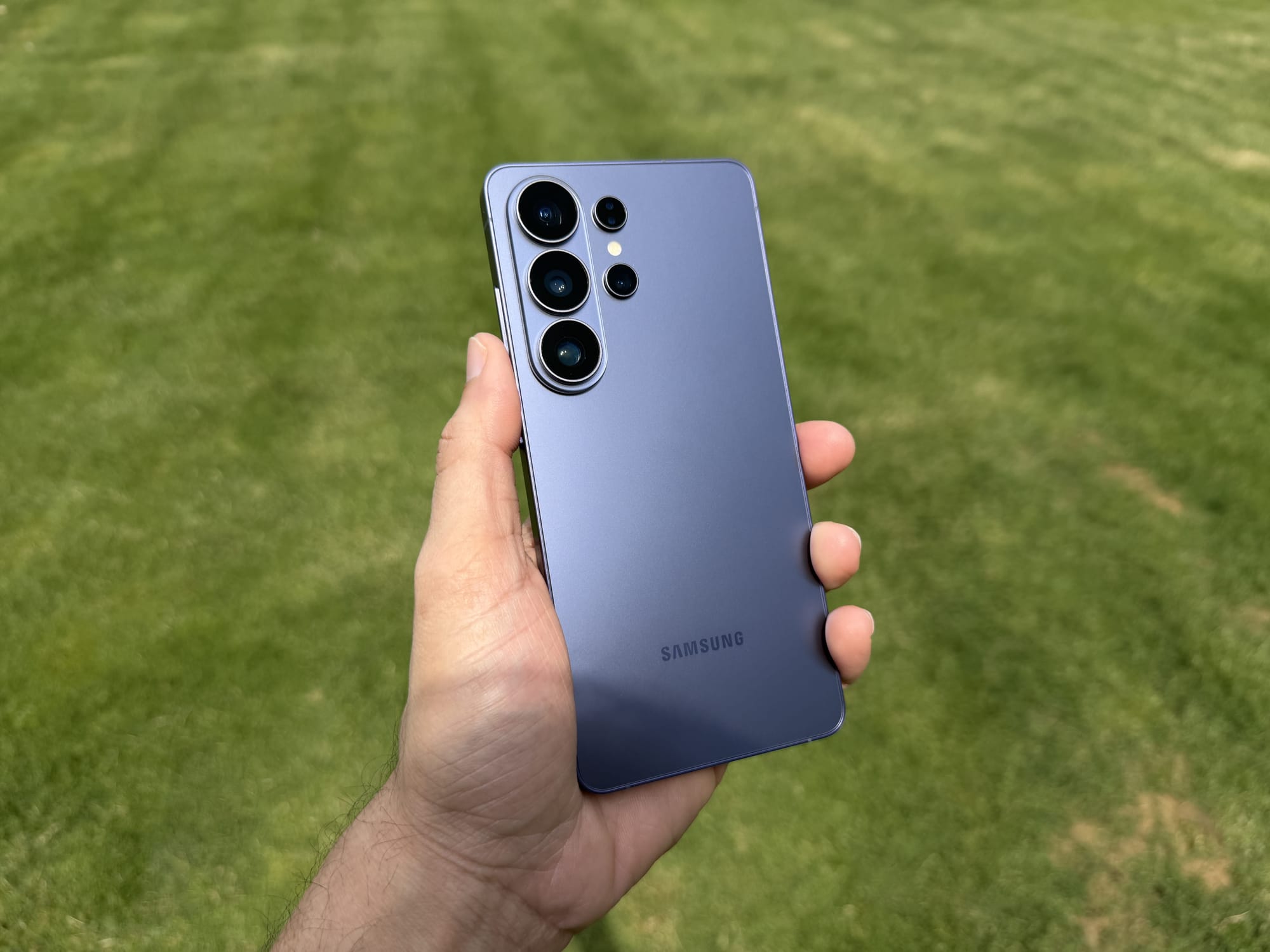 Samsung S26 Ultra in hand, showcasing its back and camera array on a grassy background.